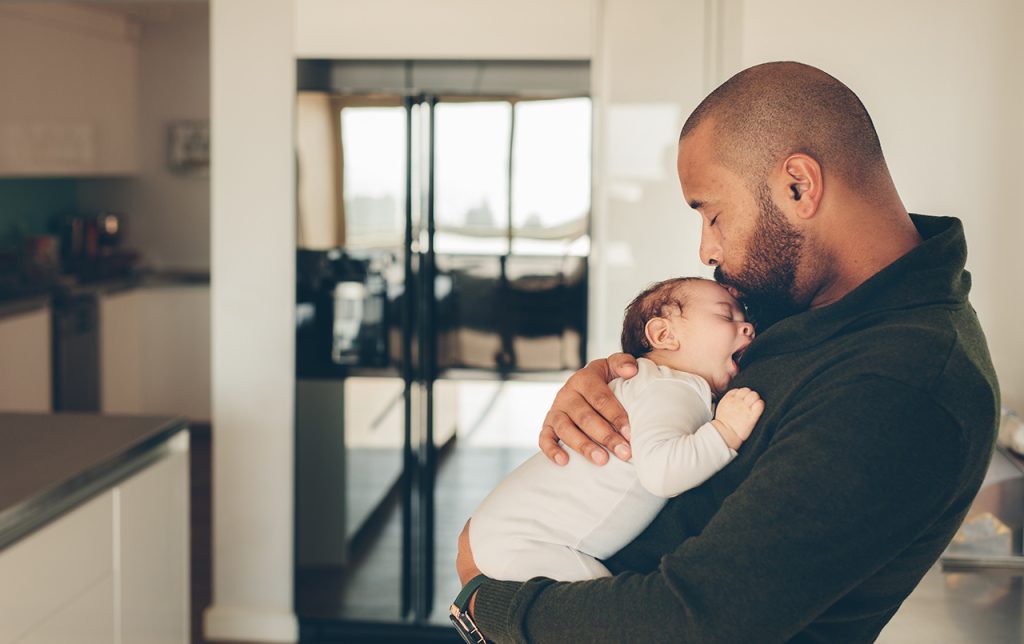 Man carrying his newborn son and kissing on his forehead. Cute little boy in his father's arms.