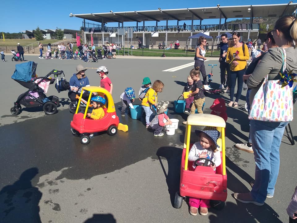 Children with their carers playing on a cement carpark with ride on toys etc