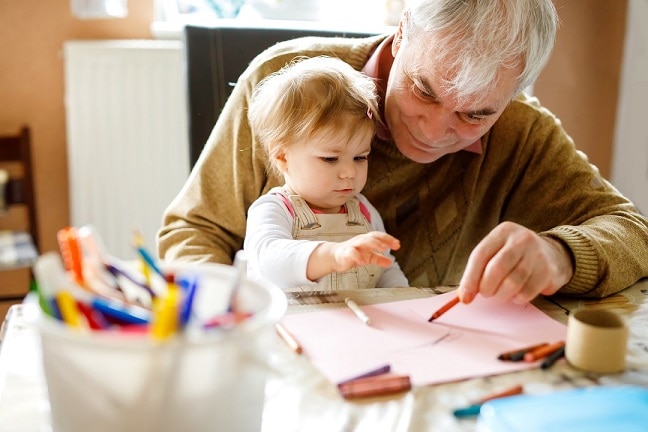 A grandfather drawing with his baby grandchild smiling