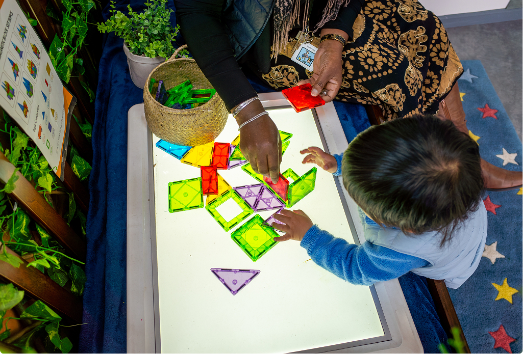 A young child playing with magnetic shapes on a light box