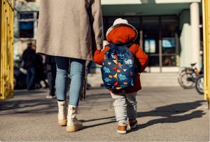 A little child holding hands with their mother walking towards a building