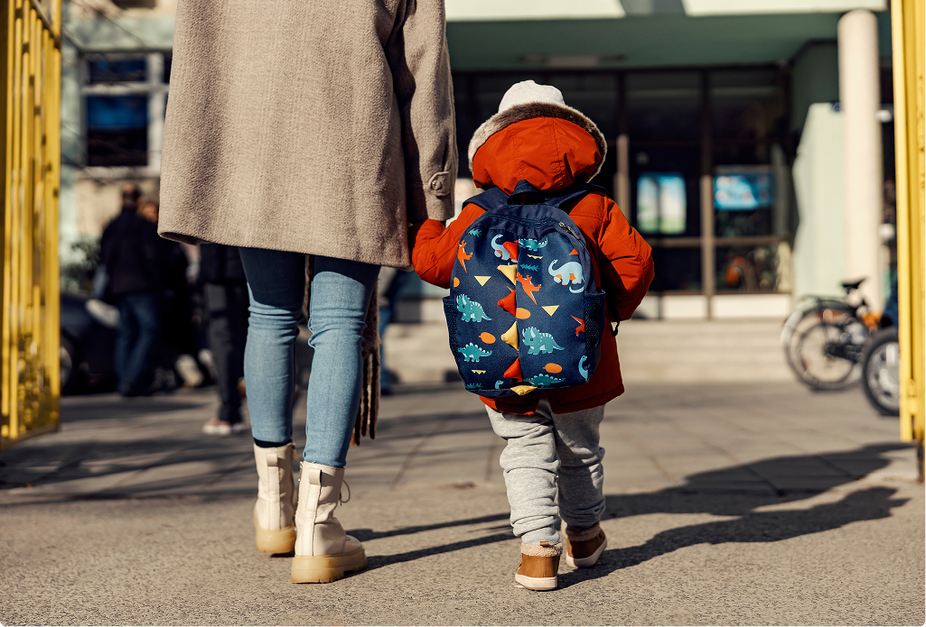 A little child holding hands with their mother walking towards a building