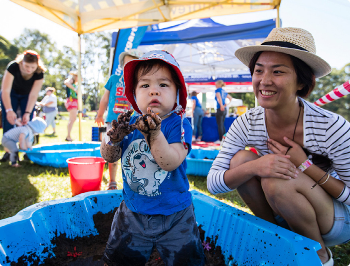 a mother smiling looking at her child playing in a muddy sandpit