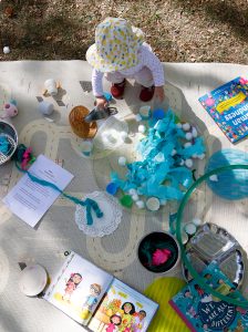 A young child sitting on a rug outside playing with craft items