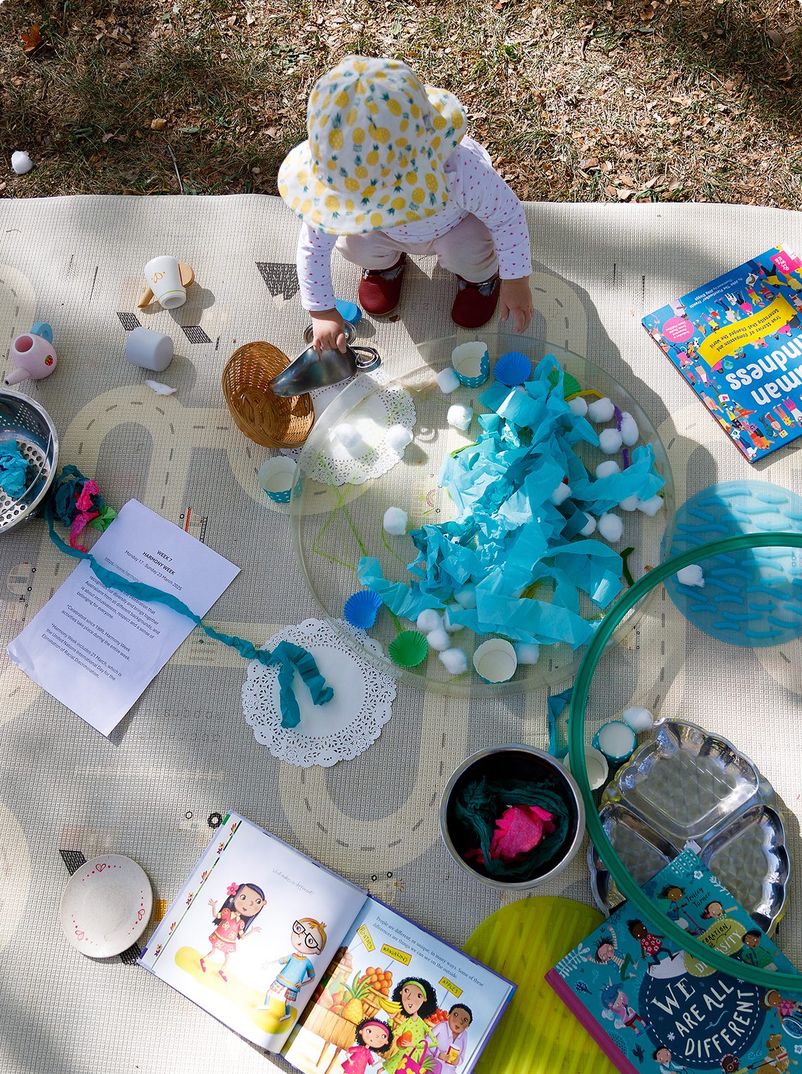 A young child sitting on a rug outside playing with craft items